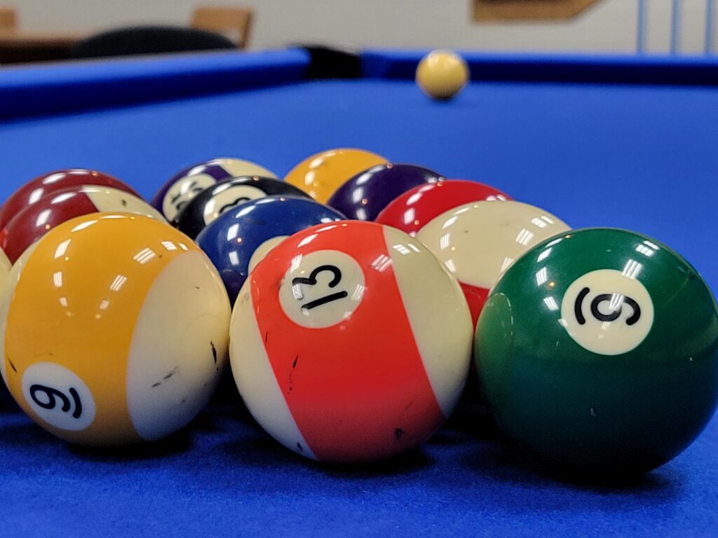 A shot of a pool table with a blue surface showing the set of racked balls with the cue ball in the background
