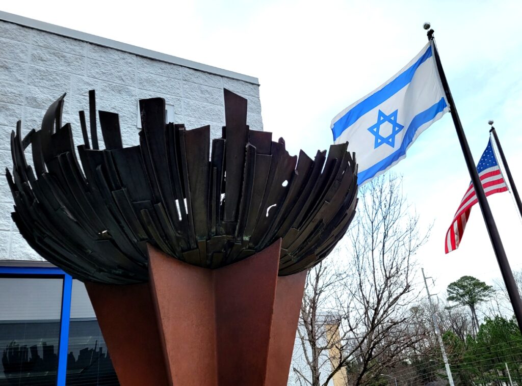 A serated sculpture on a pedestal stands in front of the Israeli and U.S. flags
