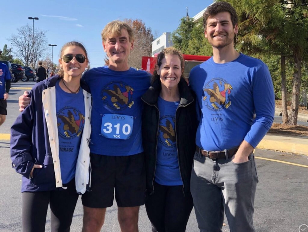 The Lapidus family of two men and two women pose for the camera on the morning of a Sam Lapidus Montclair Run while all wearing the same blue race shirt.