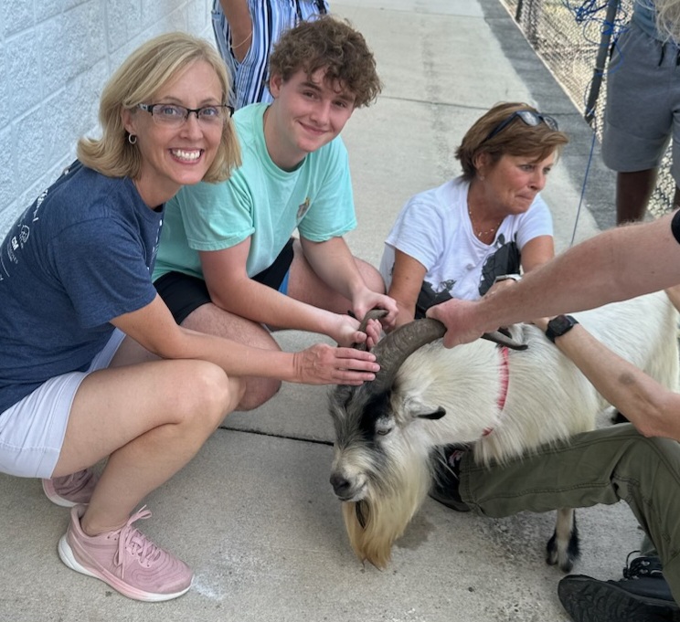 A group of people sit on the ground while securely but gently restraining a goat that had been roaming around the neighborhood for a week before being caught at The J.