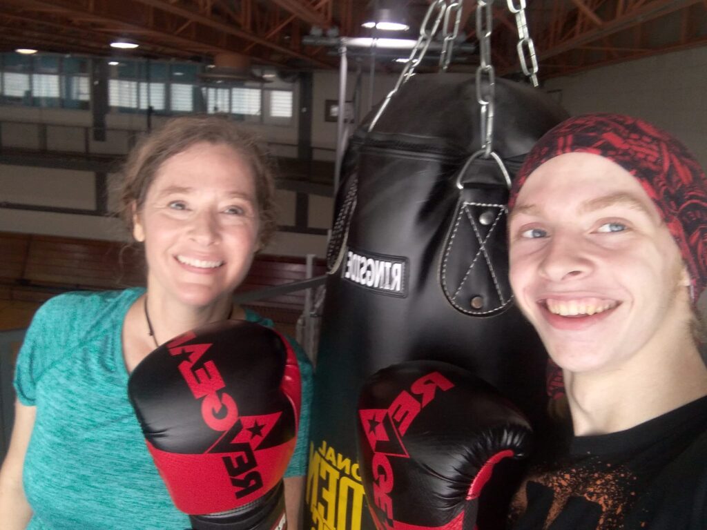 A woman and her son wearing boxing gloves flank a punching bag