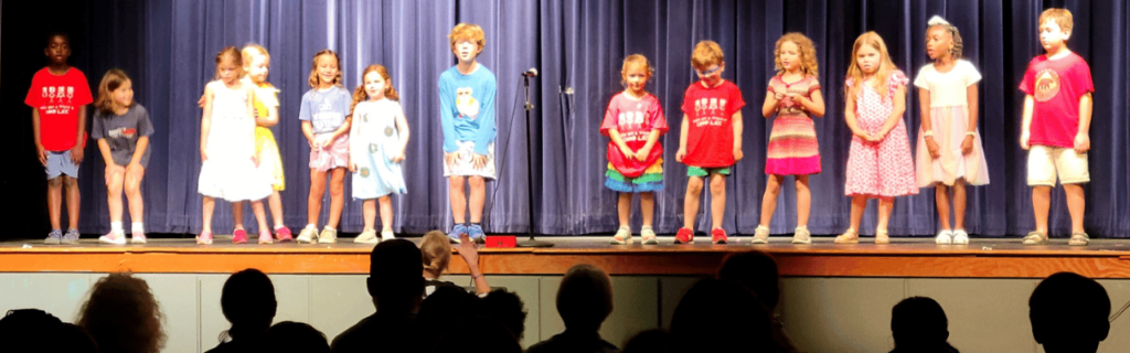 A line of children on a stage perform songs as part of a camp theater class.